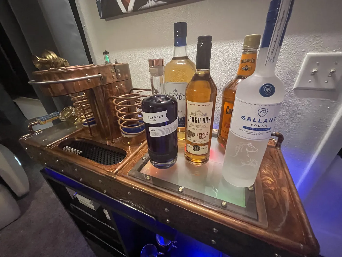 The serving tray end of the machine with three bottles standing on it, hammered-copper skirt and blue underlight