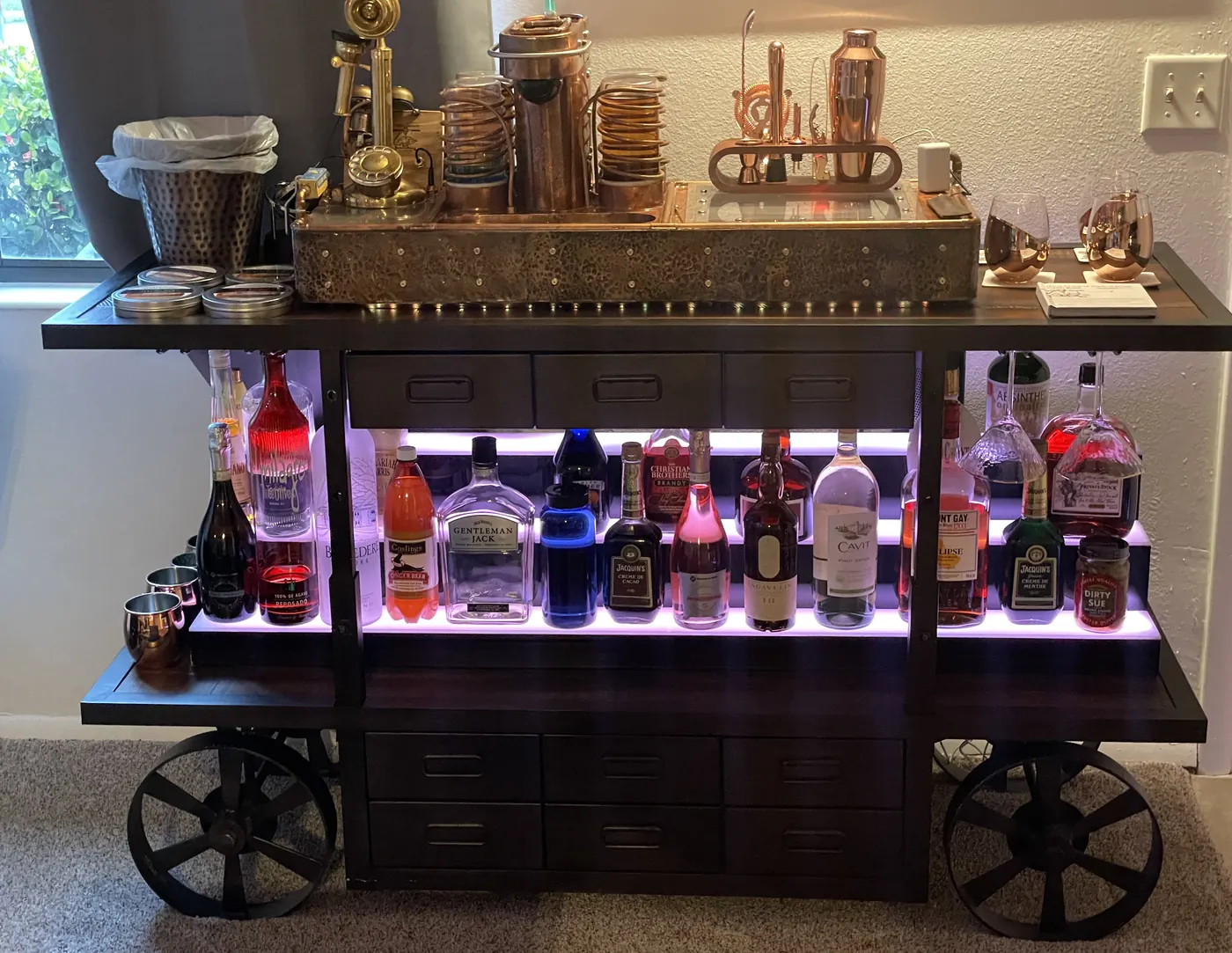 The machine on top of a wheeled industrial bar cart with a lit shelf of bottles beneath