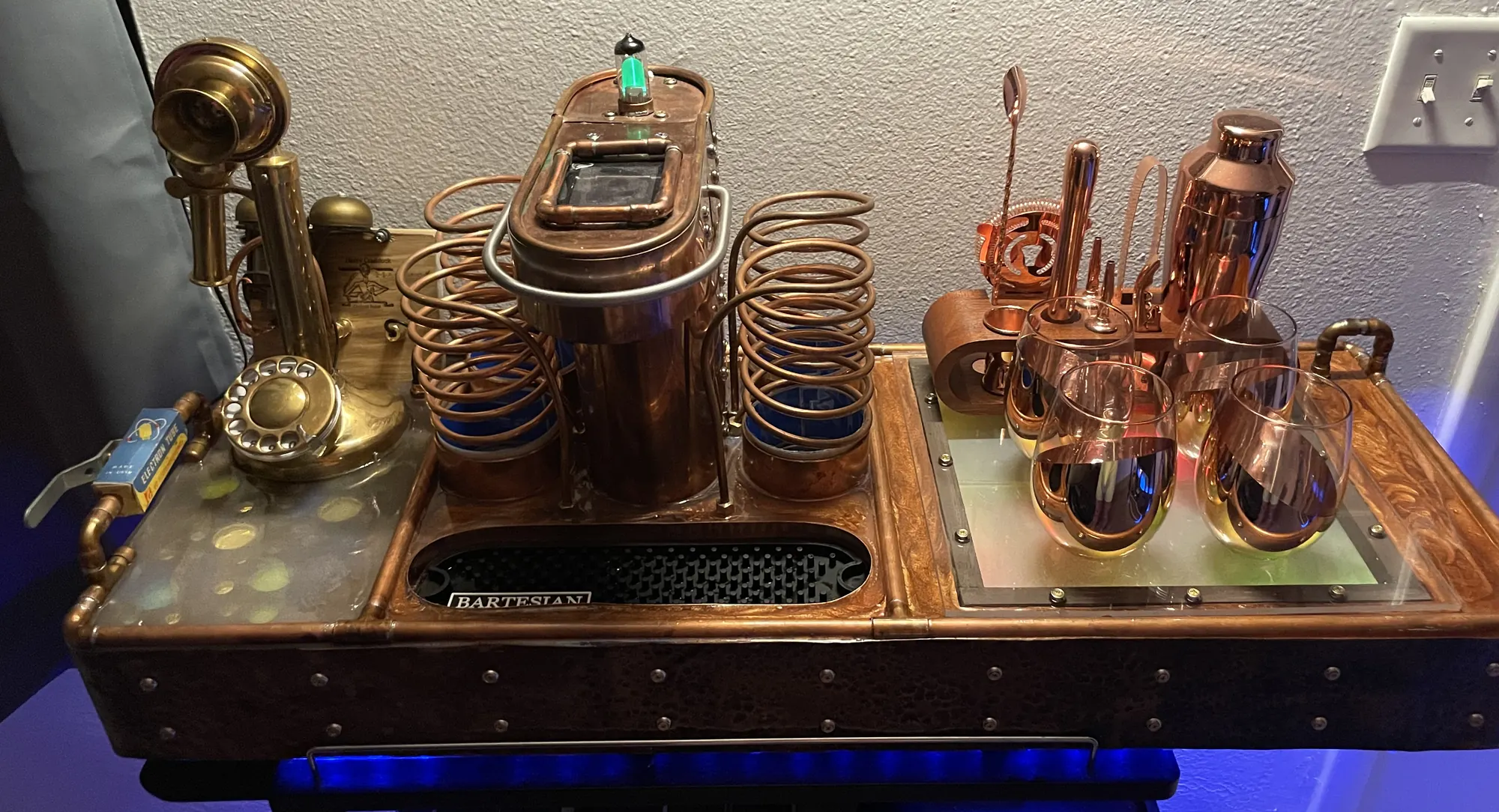 The Harry Craddock Cocktail Robot: a copper and brass cocktail machine with a candlestick telephone, glass reservoirs wrapped in copper coils, a hammered-copper skirt and blue light beneath