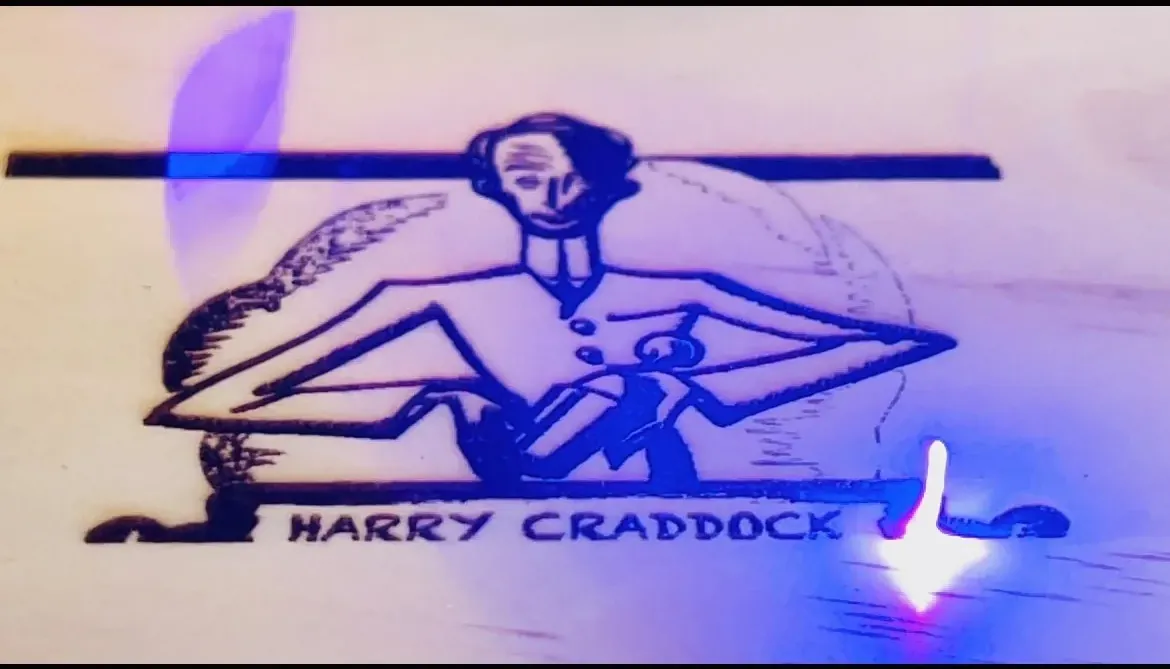 Harry Craddock's illustrated mark laser-etched into wood, lit blue