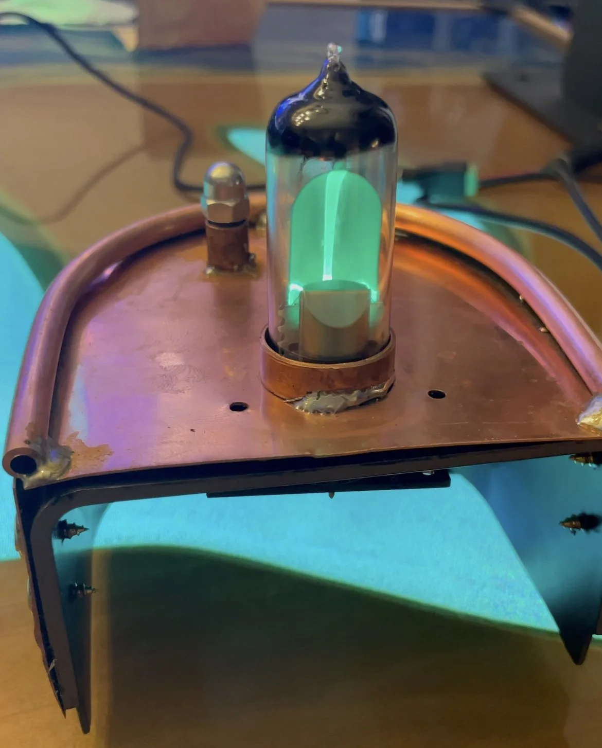 A Soviet 6E1N electron-ray tube glowing green, mounted in a copper cradle