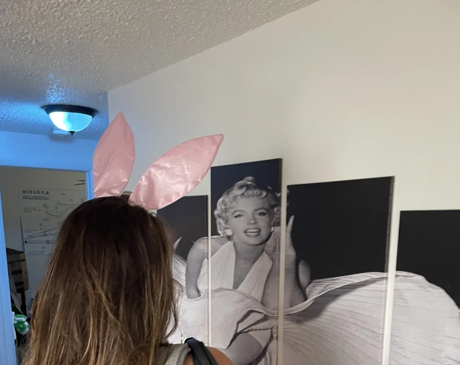 A guest in pink bunny ears facing the Marilyn Monroe wall art